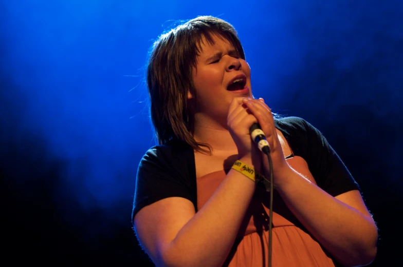 a young woman holding a microphone with blue light coming from behind her