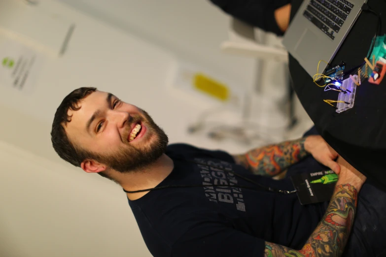 a man wearing a necklace and smiling while using his laptop