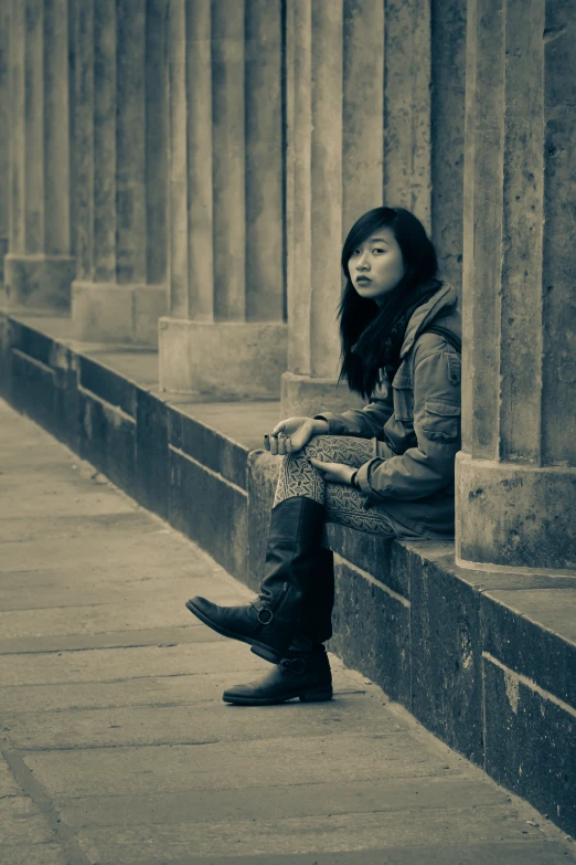 a woman sits on the side of a wall near columns