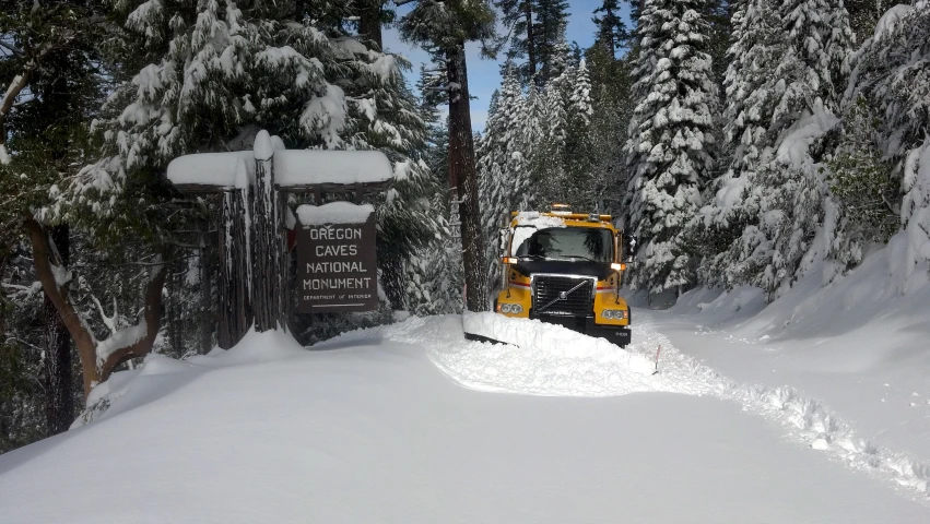 a snow plow drives past an entrance to the forest