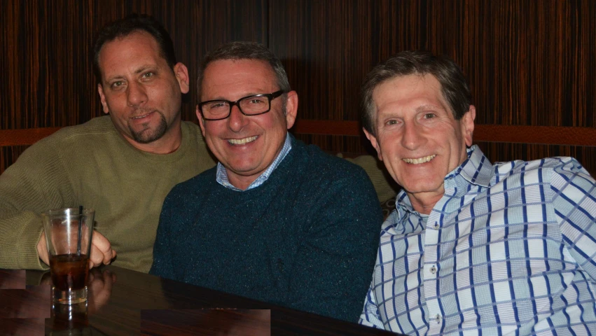 three men sitting at a bar smiling at the camera