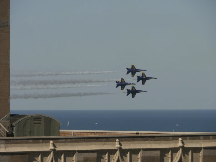 four fighter jets flying over a large building and a body of water