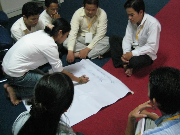 five people sitting on the floor looking at a sheet of paper