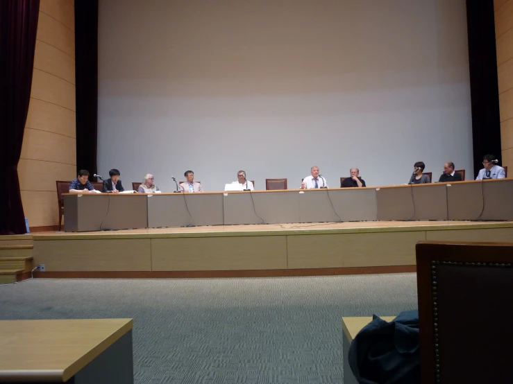 a group of people sit at tables behind the backs of chairs