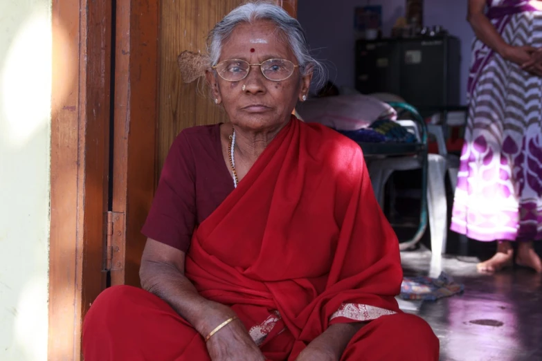 an older woman is sitting and wearing a red outfit