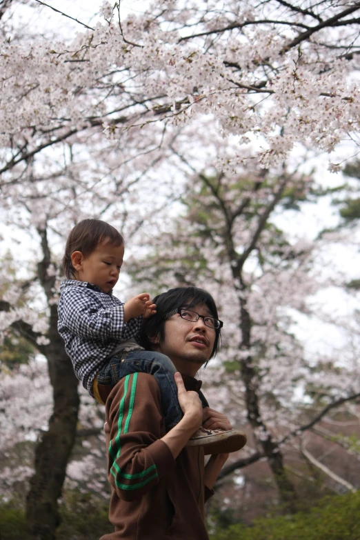 man and a child in front of some trees with blossom