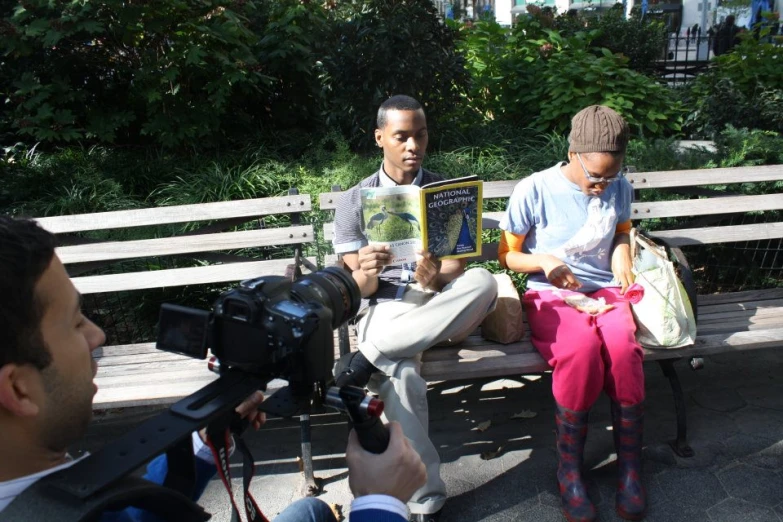 two young men are sitting on a bench reading books