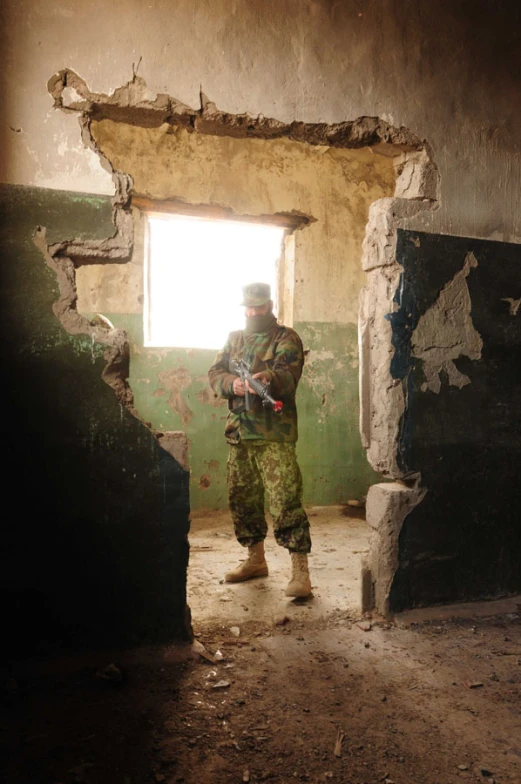 the soldier stands near a doorway as he holds his rifle