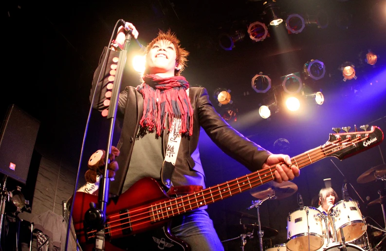 a man in black jacket and scarf playing bass guitar