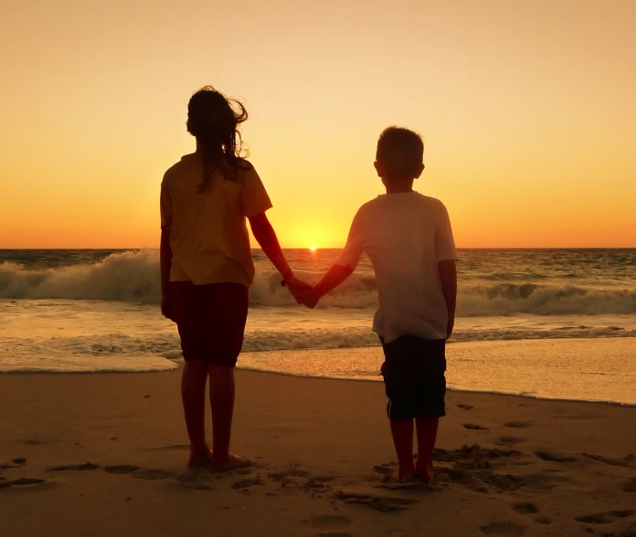 two people holding hands, with the sun setting in the background