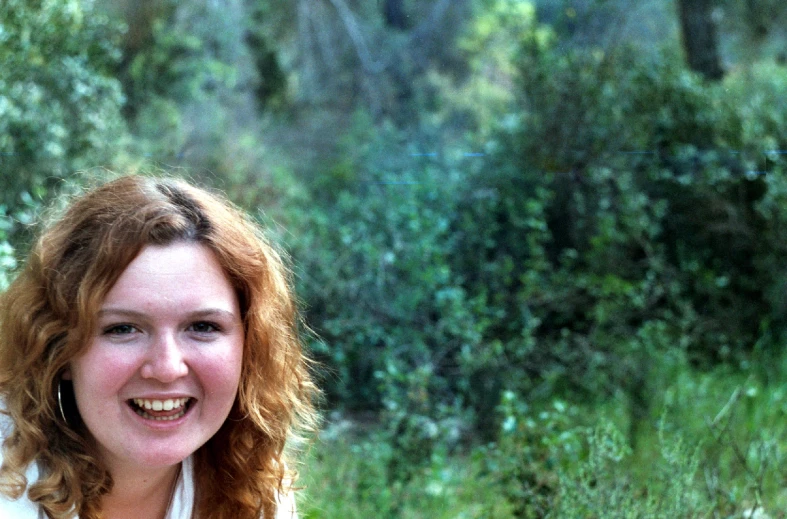 a woman standing smiling in front of a bush