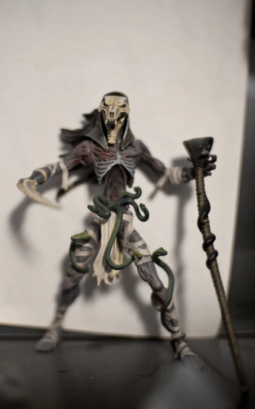 a plastic demon holding a stick with snakes on it
