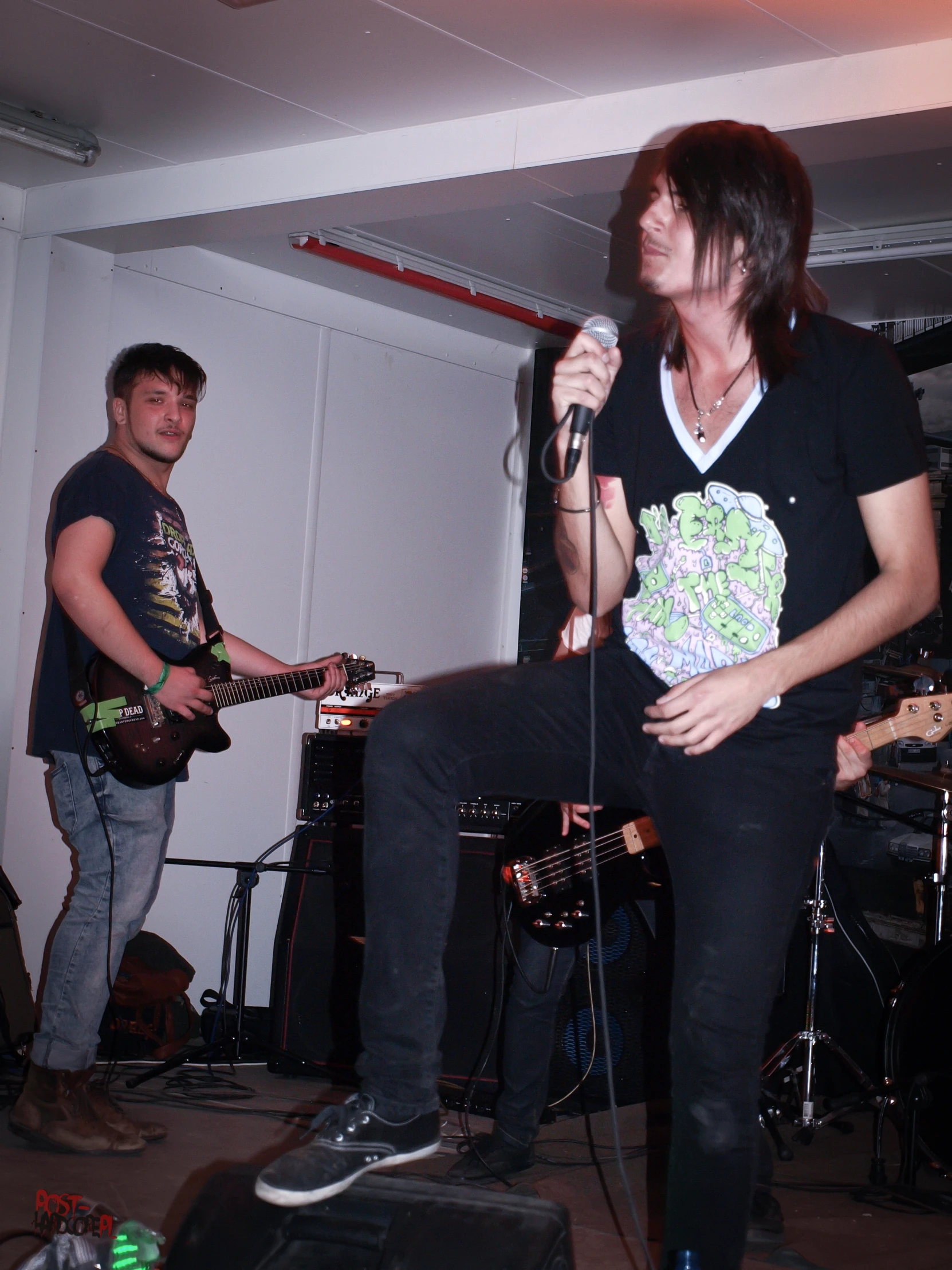 two men in the same room one of which is holding a microphone and the other one wearing a flowered shirt with an embellum