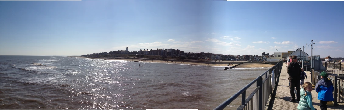 people on the pier by the ocean and one person surfing