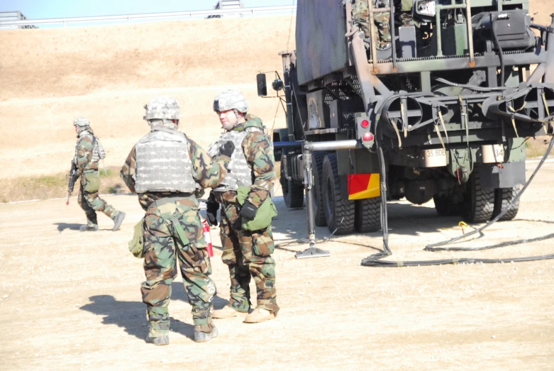 three soldiers in camouflage uniforms stand next to a military truck