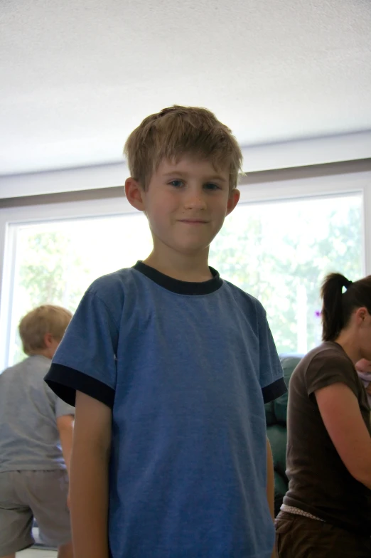 a boy wearing blue with a blue t - shirt, standing in a kitchen