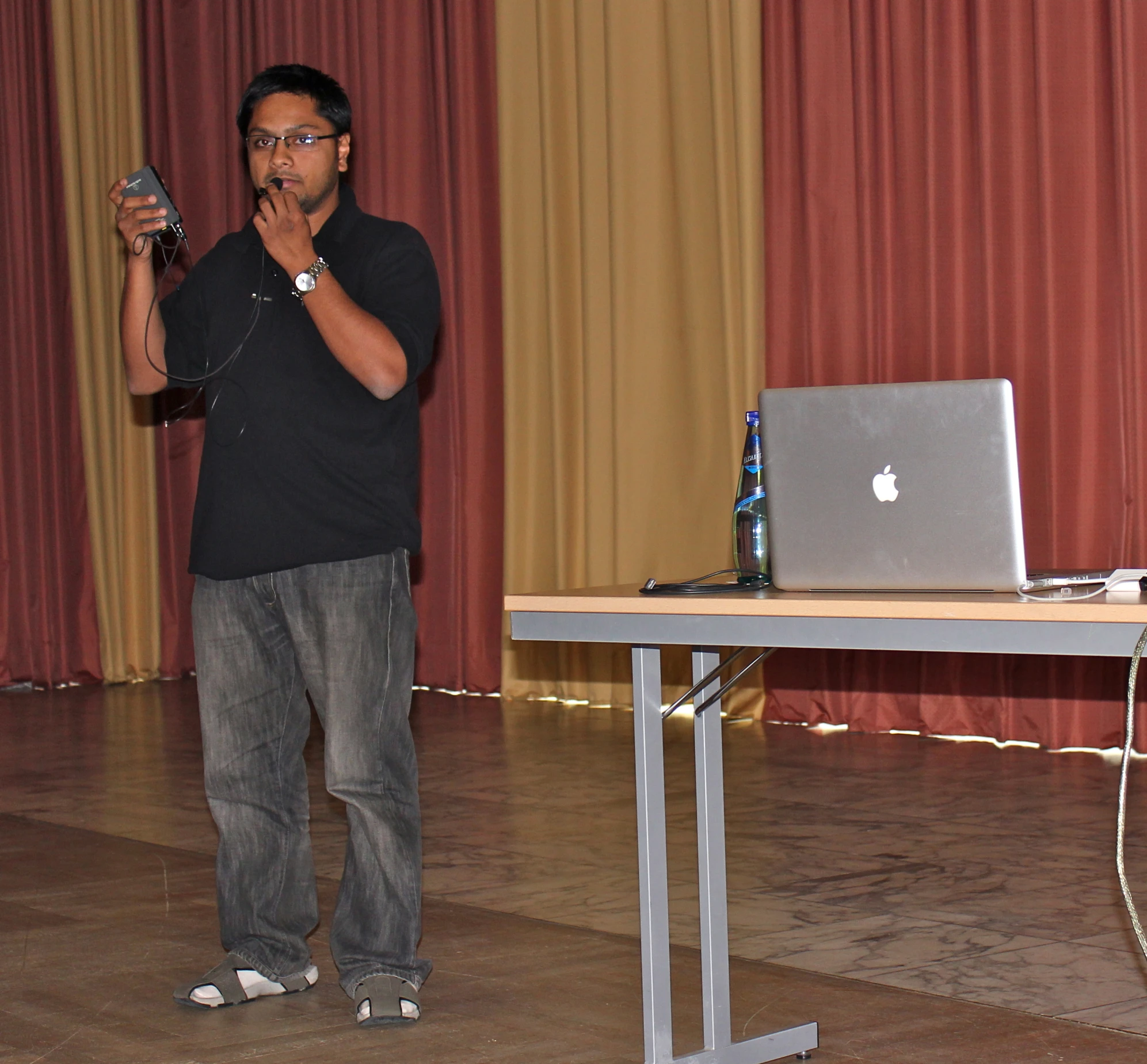 a man holding an ipod in front of a table with a laptop