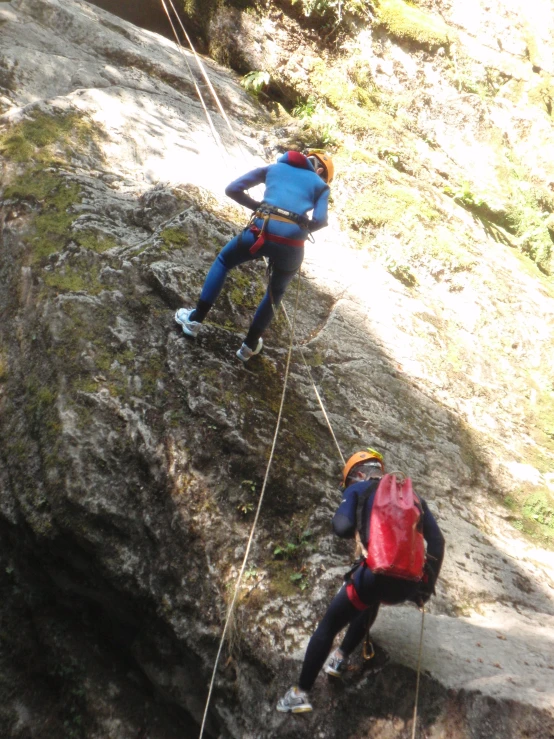 two people climbing up a cliff, one is hanging on the rope