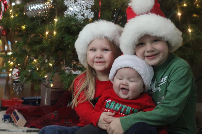 two children pose for the camera wearing christmas hats