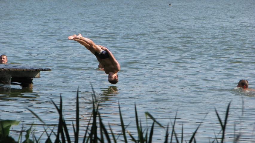 a man dives into the water while others swim in the distance
