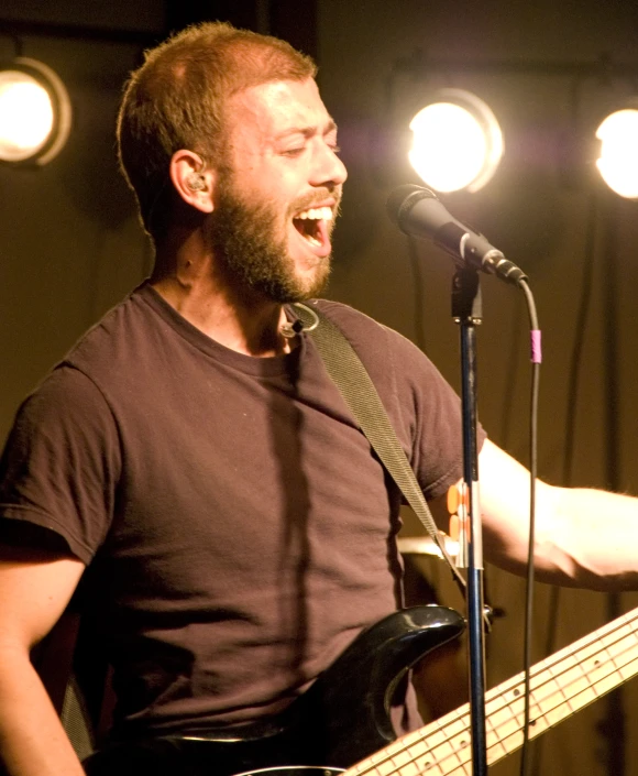 a man smiling and holding a guitar at a microphone