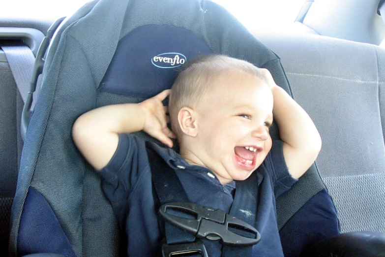 a smiling baby in a blue shirt is in a car