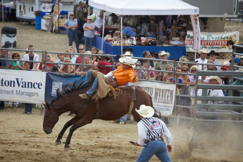 the man in orange shirt is riding a horse