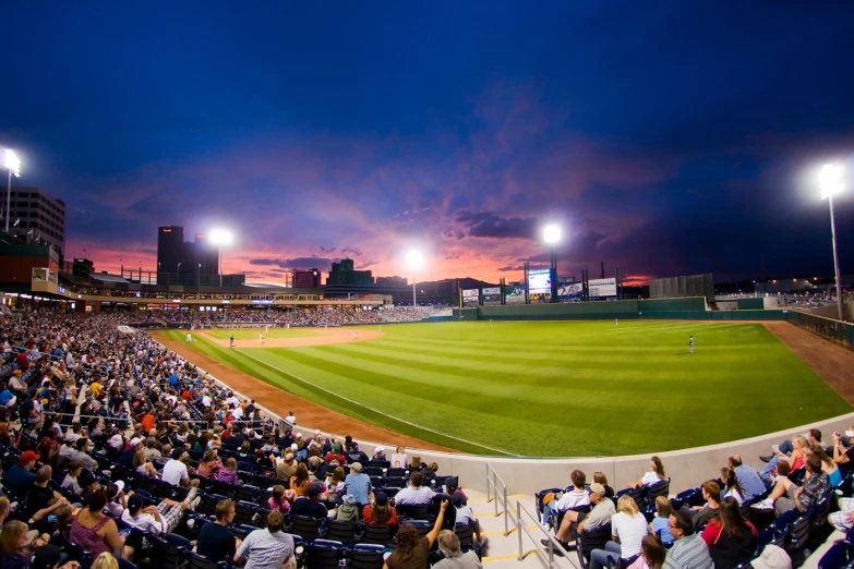 a baseball stadium filled with fans and illuminated by the sunset