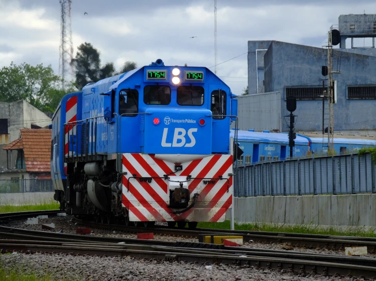 a blue train on a track with a building in the background