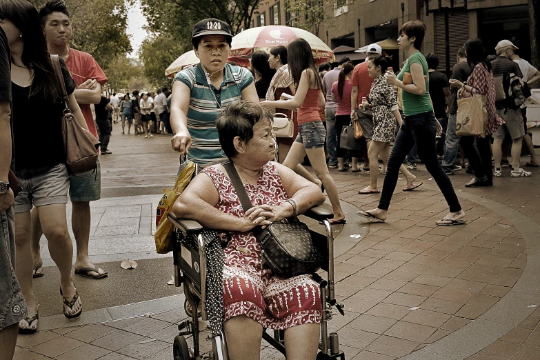 an old woman with a baby in a wheelchair and a man in a baseball cap sitting under umbrellas