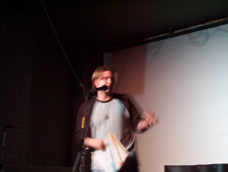 man speaking into microphone at event near projector screen