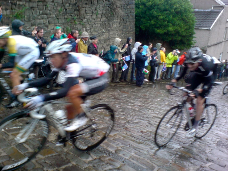 two bicyclists racing on cobblestone street with crowd