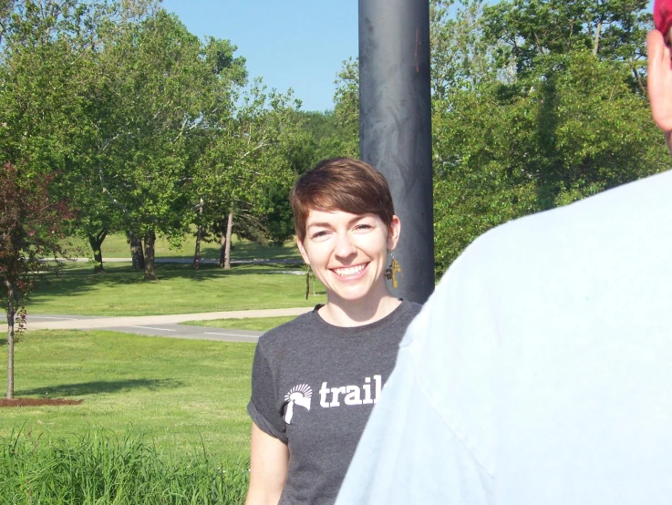 two people standing near one another with grass and trees in the background