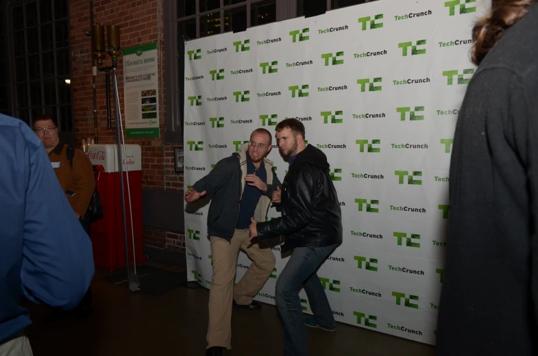 two men are playing around in front of a white poster