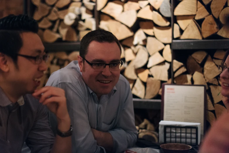 three people laughing as they talk in front of firewood logs