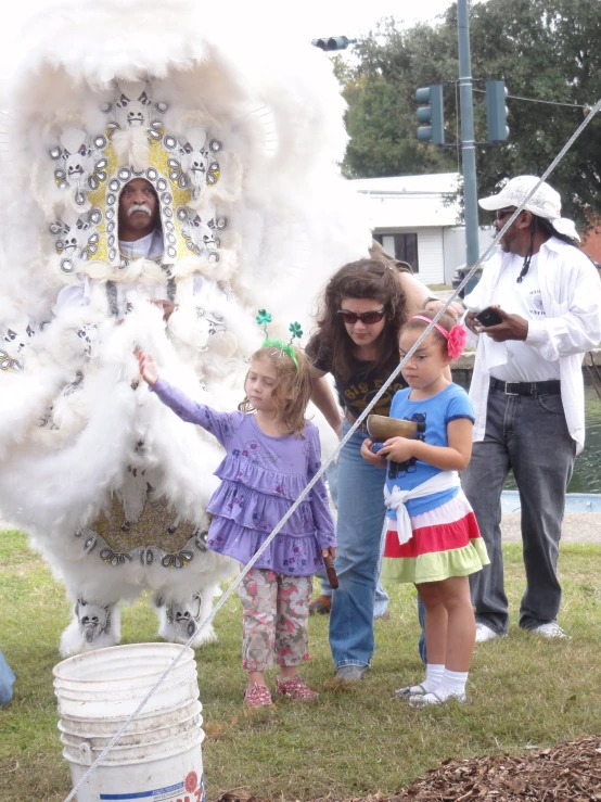 woman in a feathered suit and a small girl and boy stand next to a display of feathers and drum