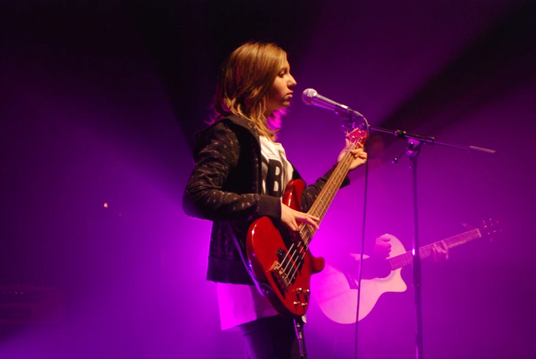 young woman playing a guitar on stage with microphone in background