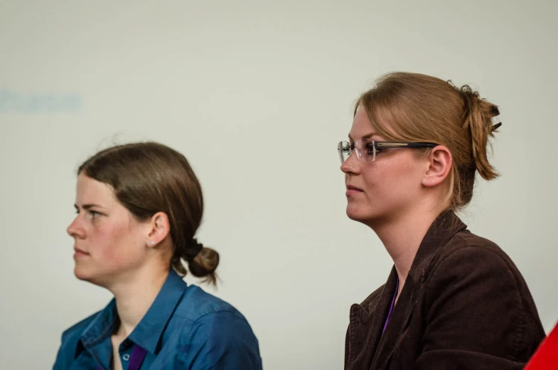 two women sitting side by side with their heads turned to the side