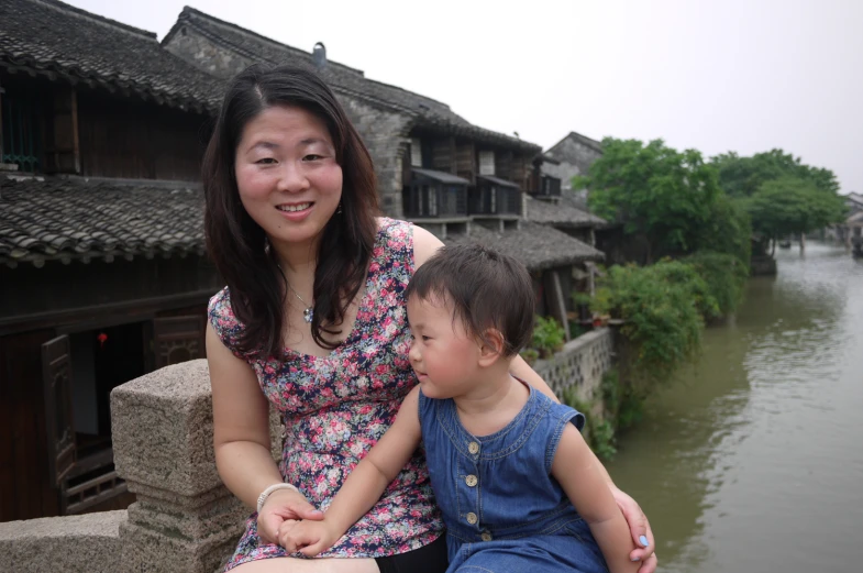 woman sitting on cement wall next to small child