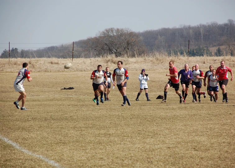 a group of young men running across a dry grass covered field