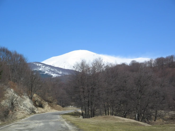 snow covered mountain towering over grassy field and roadway