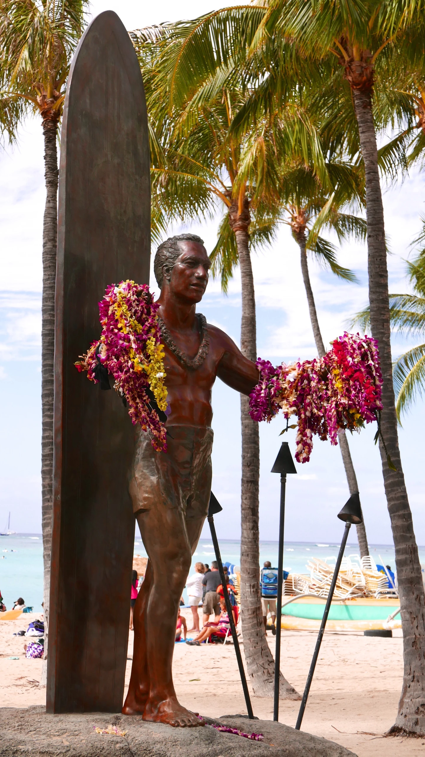 a statue stands next to a surfboard on the beach