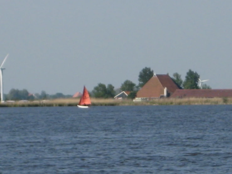 an orange sail boat in the water by some windmills