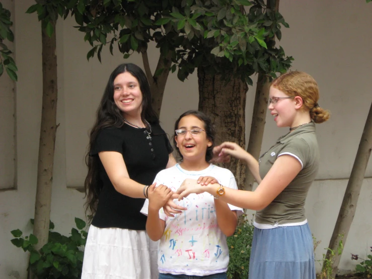 three young women standing together in front of some trees