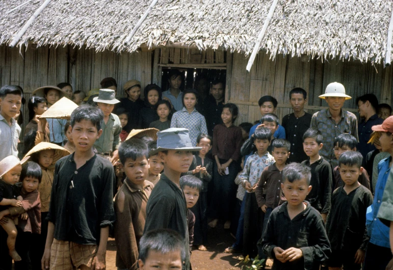 many children in front of a hut with straw roofs