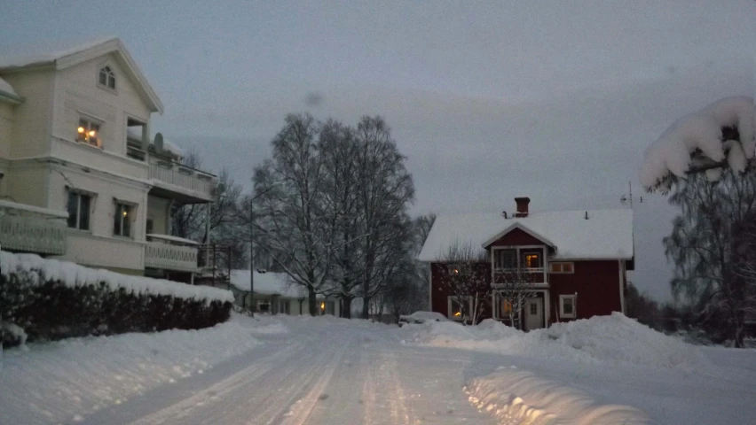 there is snow all over the street with houses and cars