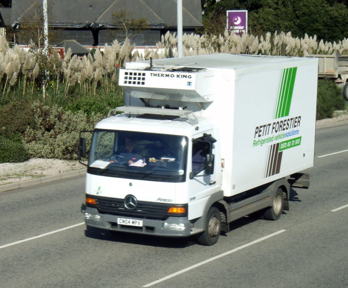 a white truck driving down the street past tall grass