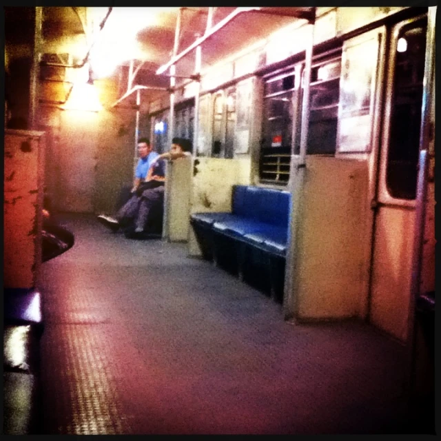 people sitting on an enclosed train car, with their backs turned to the opposite direction