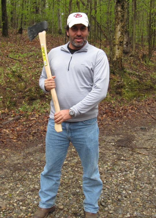 a man wearing jeans, a white cap, and a baseball glove holds a large wooden stick