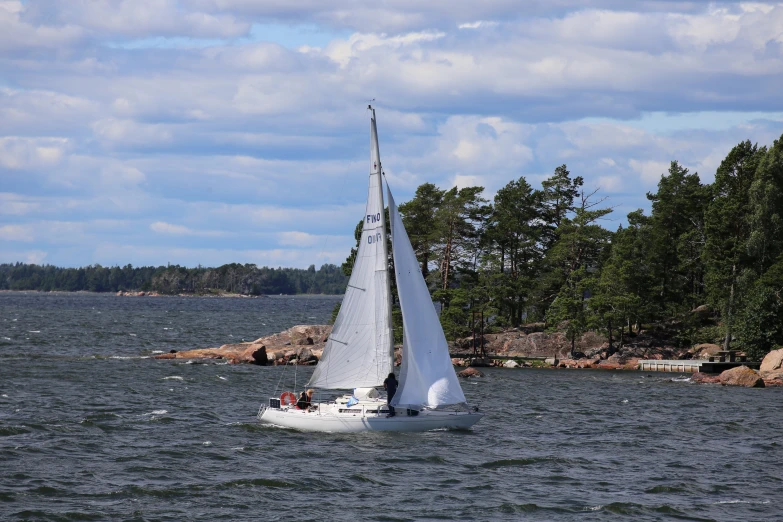 sailboat with white sails cruising on water near rocky shoreline